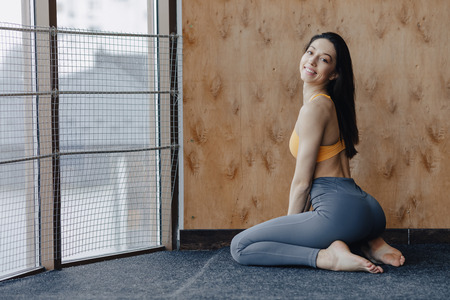 Young attractive fitness girl sitting on the floor near the window on the background of a wooden...