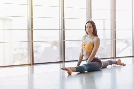 cozy young attractive girl doing fitness exercises with yoga on the floor against the background of panoramic windowsの写真素材