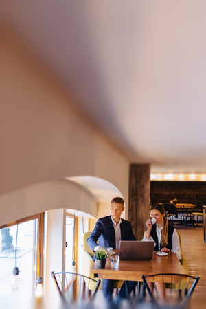 A stylish couple drinks morning coffee at the cafe with cozy interior and works with a laptop, young businessmen and freelancersの写真素材