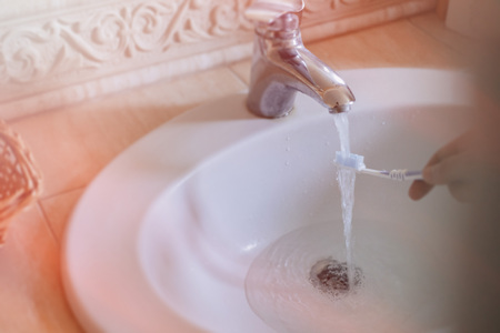 washing the toothbrush under the water flow in the washbasin, morning hygieneの写真素材