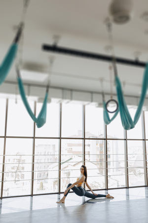 cozy young attractive girl doing fitness exercises with yoga on the floor against the background of panoramic windowsの写真素材