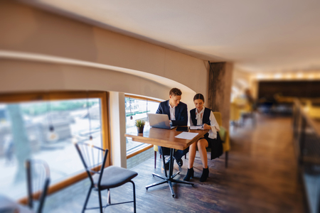 young businessmen boy and girl work with a laptop, a tablet and notes in the cafe with cozy interiorの写真素材