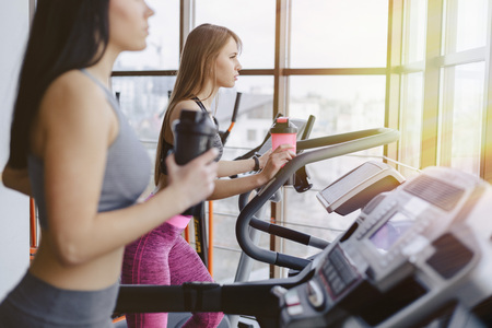 Girls in the gym are trained on treadmills and drink water, smiling and healthy