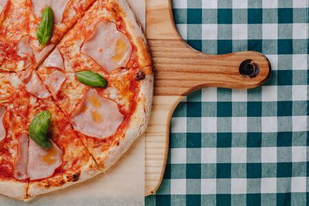 Neapolitan pizza on a cream sauce with ham, cheese, arugula, basil, tomatoes sprinkled with cheese on a wooden board on a tablecloth in a cell with a place for textの写真素材