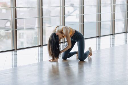 cozy young attractive girl doing fitness exercises with yoga on the floor against the background of panoramic windowsの写真素材