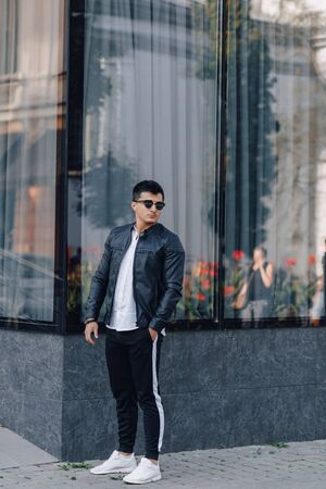 young stylish guy in glasses in black leather jacket on simple glass backgroundの写真素材