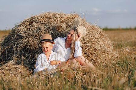 pretty blond long-haired woman with little blond son at sunset relaxing in the field and savoring fruit from a straw basket. summer, farming, nature and fresh air in the countryside. sunset.の写真素材