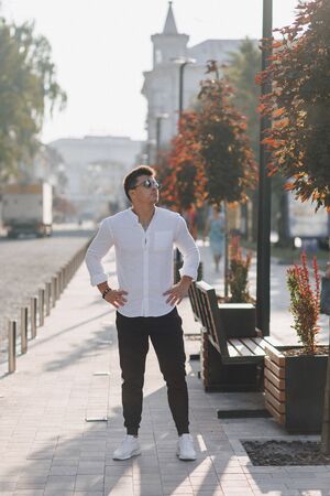 young stylish guy in a white shirt walking down a European street on a warm sunny dayの写真素材