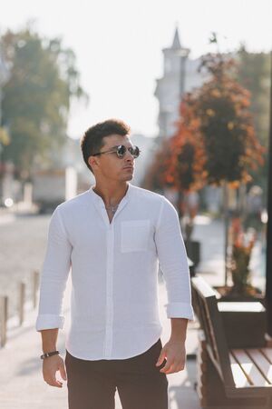 young stylish guy in a white shirt walking down a European street on a warm sunny dayの写真素材