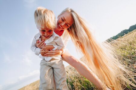 blond little boy playing with mom with white hair with hay in field. summer, sunny weather, farming. happy childhood. family.の写真素材