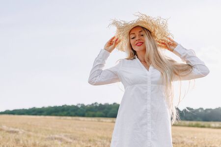 pretty woman with blond long hair in a straw hat in a field at sunset. summer, farming, nature and fresh air. sunny.の写真素材