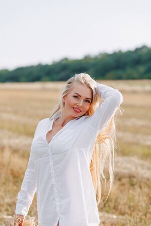 pretty woman with blond long hair in a field at sunset. summer, farming, nature and fresh air. sunny.の写真素材