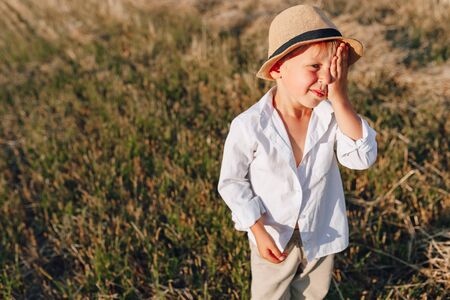 blond little boy in straw hat playing in field on mowed hay. summer, sunny weather, farming. happy childhood. sunny.の写真素材