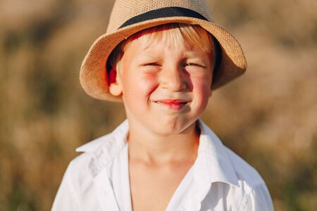 blond little boy in straw hat playing in field on mowed hay. summer, sunny weather, farming. happy childhood. sunny.の写真素材
