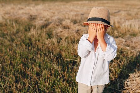 blond little boy in straw hat playing in field on mowed hay. summer, sunny weather, farming. happy childhood. sunny.の写真素材