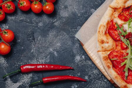 spicy appetizing Neapolitan pizza on a blackboard with cherry tomatoes and chilli, free space for textの写真素材