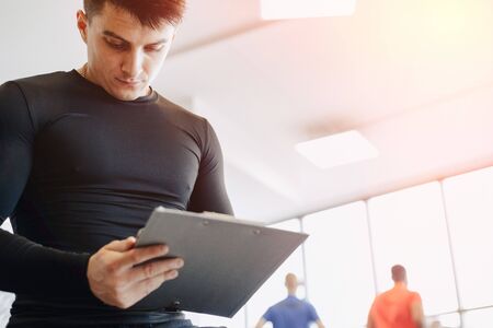 young guy trainer takes notes in the gym. personal trainer for sports. gym and sports.