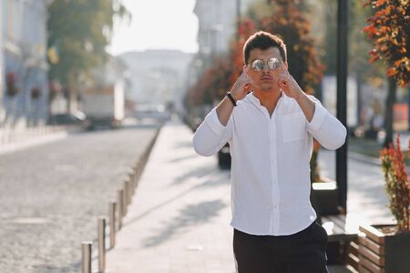 young stylish guy in a white shirt walking down a European street on a warm sunny dayの写真素材