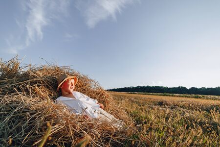 blond little boy having fun jumping on hay in field. summer, sunny weather, farming. happy childhood. countryside. sunny.の写真素材
