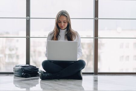 attractive girl working with laptop and things in airport terminal or office on floor. travel atmosphere or alternative work atmosphere. freelancer student travels to business meeting. concept of alternative workplace, technology and waiting.の写真素材