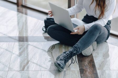attractive girl working with laptop and things in airport terminal or office on floor. travel atmosphere or alternative work atmosphere. freelancer student travels to business meeting. concept of alternative workplace, technology and waiting.の写真素材