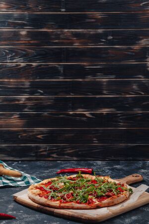 spicy appetizing Neapolitan pizza on a blackboard with cherry tomatoes and chilli, free space for textの写真素材