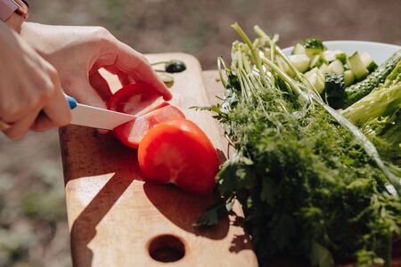girl slices vegetables on the board and prepares a salad on the nature outside. sunny day and...