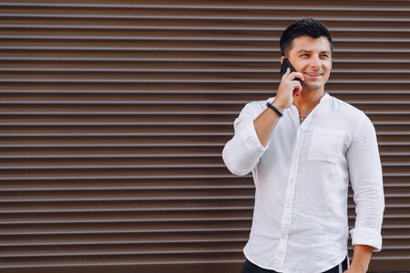 young stylish guy in shirt talking by phone on simple brown backgroundの写真素材