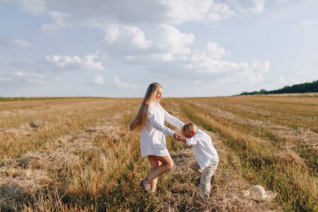 blond little boy playing with mom with white hair with hay in field. summer, sunny weather, farming. happy childhood. family.の写真素材
