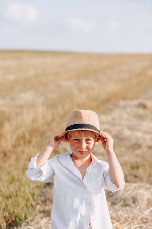 blond little boy in straw hat playing in field on mowed hay. summer, sunny weather, farming. happy childhood. sunny.の写真素材
