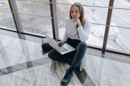 attractive girl working with laptop and things in airport terminal or office on floor. travel atmosphere or alternative work atmosphere. freelancer student travels to business meeting. concept of alternative workplace, technology and waiting.の写真素材