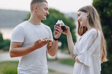 couple eating pizza and drinking in nature at sunsetの写真素材