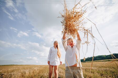 blond little boy playing with mom with white hair with hay in field. summer, sunny weather, farming. happy childhood. family.の写真素材