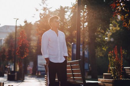 young stylish guy in a white shirt walking down a European street on a warm sunny dayの写真素材
