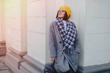 Attractive smiling young girl in stylish glasses in coat and yellow Beret on a simple light backgroundの写真素材