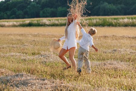 blond little boy playing with mom with white hair with hay in field. summer, sunny weather, farming. happy childhood. family.の写真素材