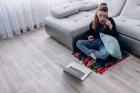 cozy young attractive girl at home working with a laptop and talking on the phone. comfort and coziness while at home. home office and work from home. remote online employment.の写真素材