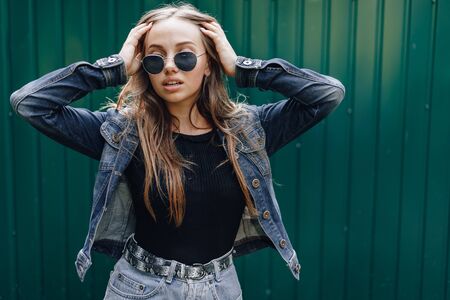 young pretty attractive girl in denim clothes in glasses on a simple dark green background with empty place for text.の写真素材
