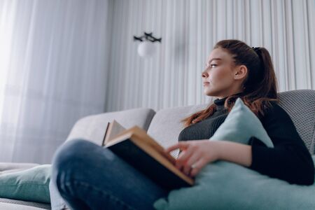 young attractive girl on the couch reads a paper book. mental development. useful use of time at...