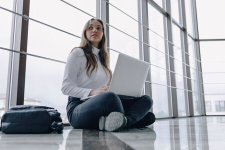 attractive girl working with laptop and things in airport terminal or office on floor. travel atmosphere or alternative work atmosphere. freelancer student travels to business meeting. concept of alternative workplace, technology and waiting.の写真素材