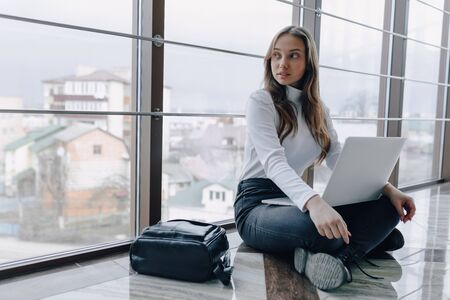 attractive girl working with laptop and things in airport terminal or office on floor. travel atmosphere or alternative work atmosphere. freelancer student travels to business meeting. concept of alternative workplace, technology and waiting.の写真素材