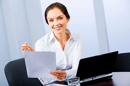 Portrait of beautiful secretary sitting at the table and holding a paper, pen の写真素材