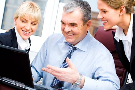 Portrait of senior boss and two young businesswomen looking at the laptop monitor with smiles on the background of office windowの写真素材