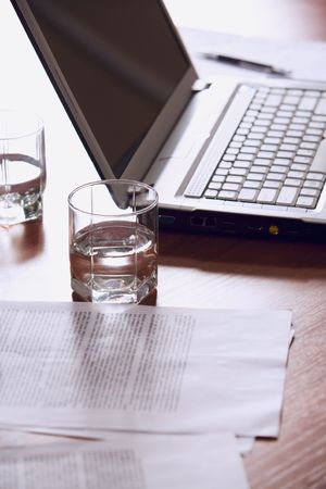 Customary workplace: laptop, papers, pen and glasses of water on a table.の写真素材