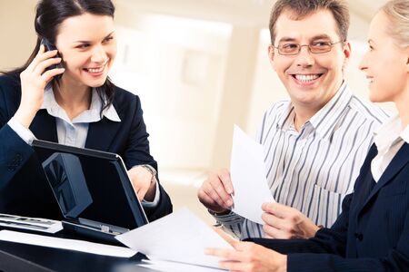 Group of three business people sitting and looking at each other with smiles during workの写真素材