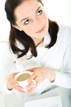 Vertical image of smart business lady looking up and holding cup of coffee in handsの写真素材