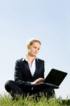 Businesswoman sitting with laptop and looking at its screen outside の写真素材