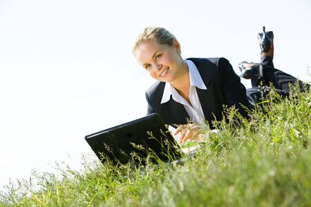 Portrait of businesswoman lying on green grass with laptop near by and looking aside の写真素材
