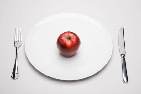 Image of red apple on white plate with fork and knife near byの写真素材