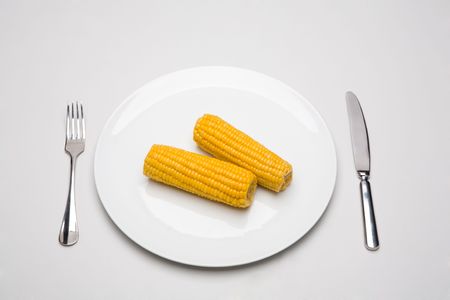 Photo of two cobs placed on the plate with fork and knife near byの写真素材